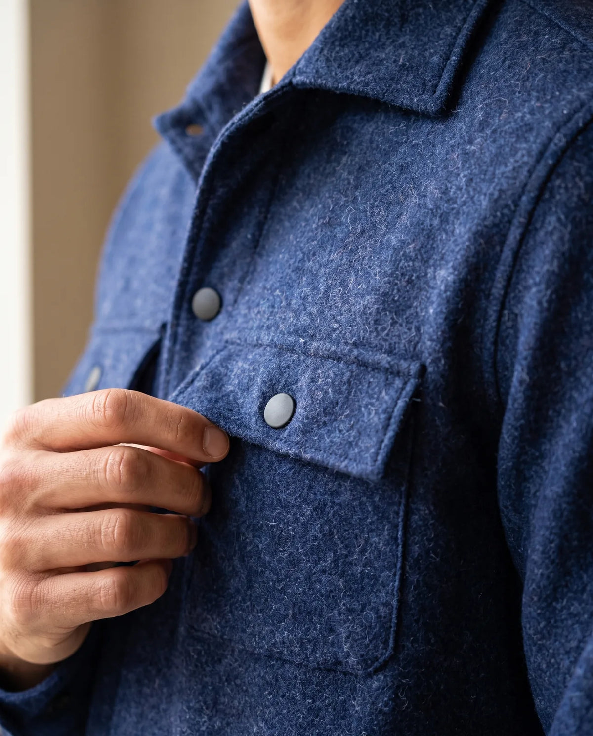 Detalle del bolsillo con tapa y botón de la chaqueta de paño azul oscuro
